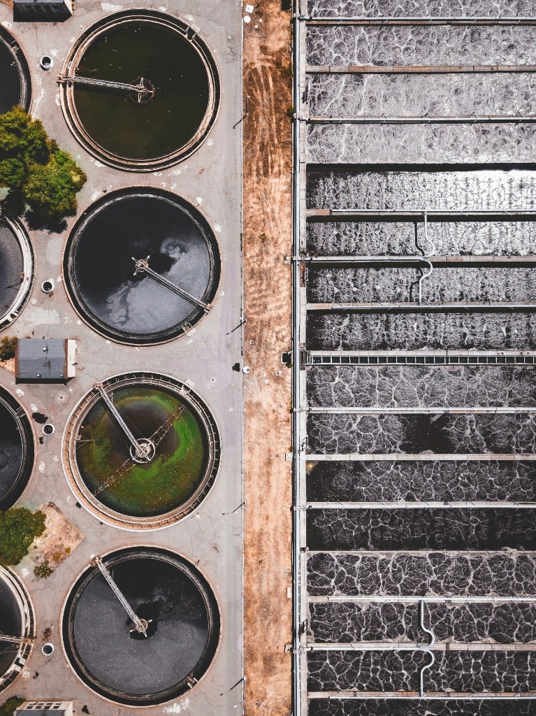 Aerial view of circular clarifiers beside long rectangular process basins at a municipal or industrial water treatment plant.